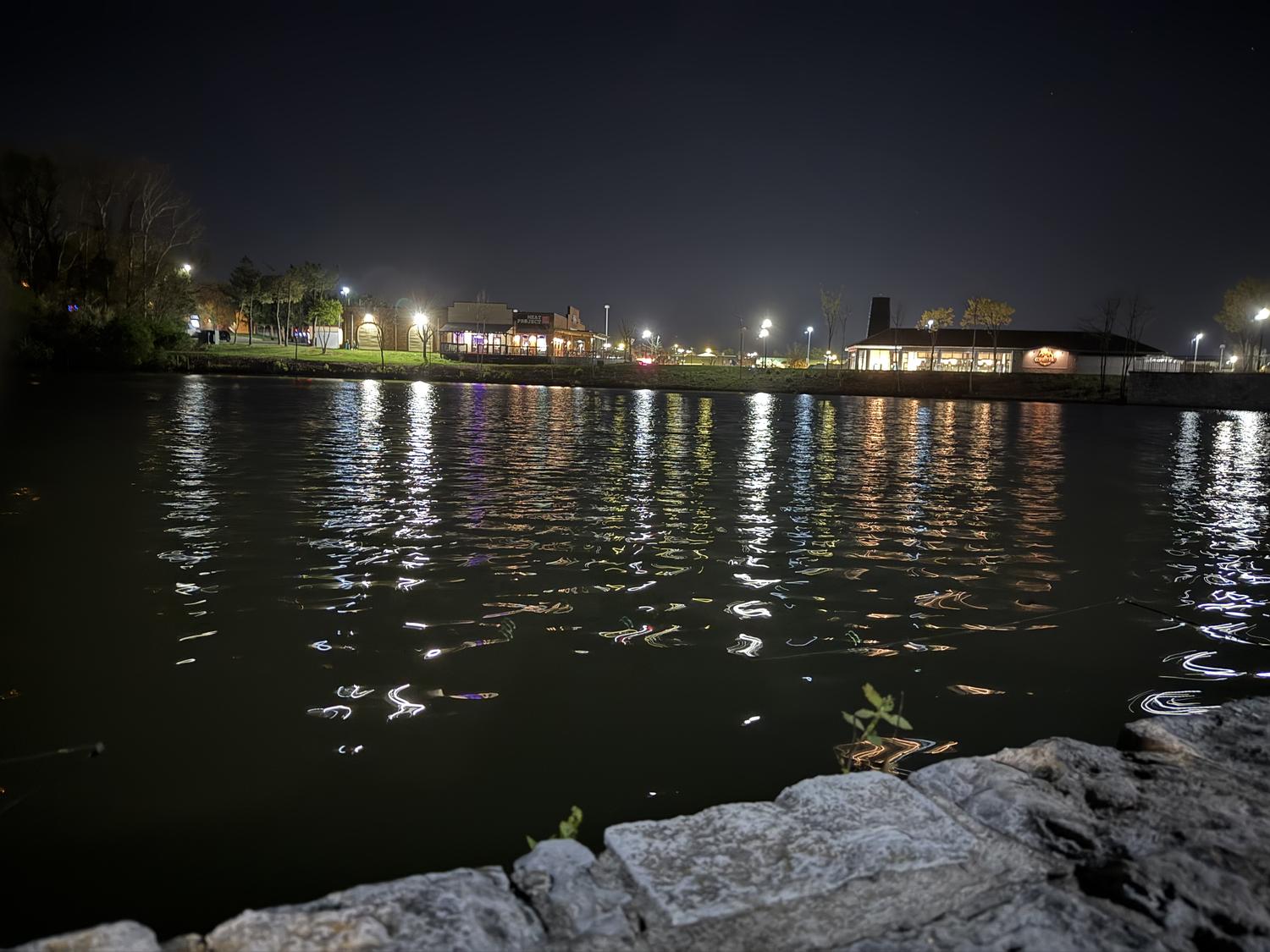 The pond at night with restaurant and street lights on the far bank reflected in long streaks across the water.